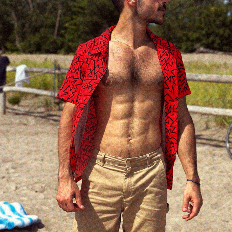Muscular man on a beach in a red 90's pattern vintage style hawaiian shirt